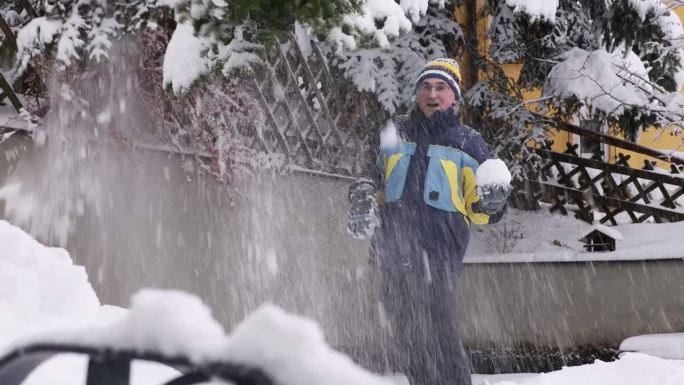 奥地利，一名男子在一个村庄的院子里，手里拿着一个雪花玻璃球，从一棵巨大的冷杉树枝上抖掉雪