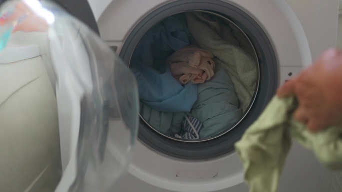 白种老年妇女把脏衣服放进洗衣机。快乐的女孩做家务坐在洗衣机前，把家里的衣服洗得脏兮兮的。