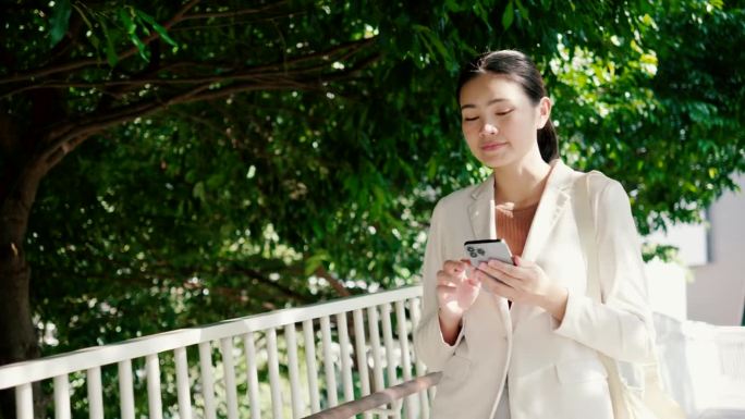 一位身穿白色西装的亚洲女商人用电话与客户沟通。位于办公室花园区域