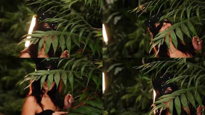 带着BDSM猫面具的性感女人在热带花园的棕榈树中摆姿势。