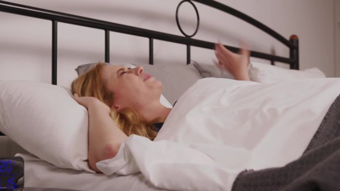 正在睡觉的中年妇女被噪音打扰，在床上用枕头蒙住头