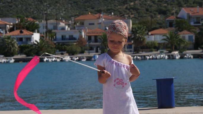 一个小女孩在希腊爱琴海的一个混凝土码头上玩着粉色的体操带