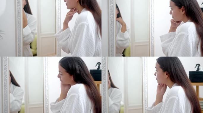 一个女人，穿着浴袍，在家里练习美容护肤程序，对着浴室的镜子审视自己