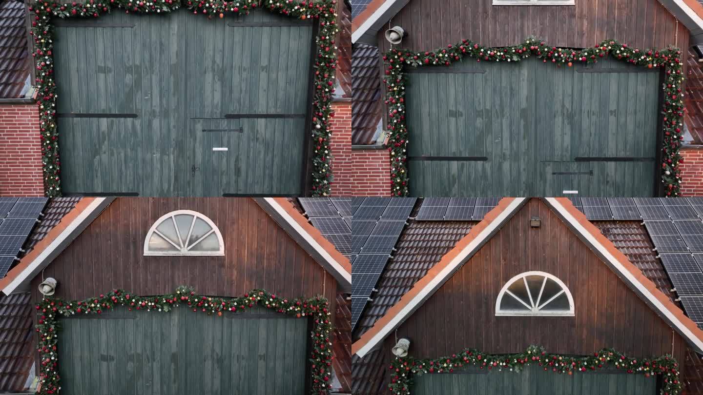 航拍的谷仓门上装饰着圣诞花环，窗户上的日出反射和谷仓屋顶上的太阳能电池板。有节日装饰的谷仓，比如星星