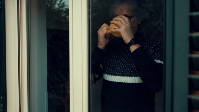 一个体贴的成年男子一边看着窗外，一边喝着热饮