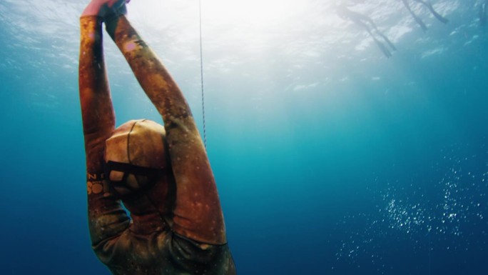 一名女子自由跳水者在绳索附近上升，摄像机围绕着模特旋转，并在水面上展示了自由跳水队