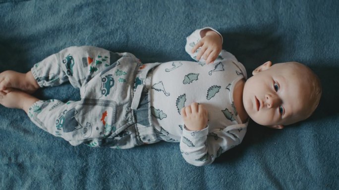 一个快乐的小男孩穿着紧身衣躺在家里柔软的蓝色毯子上。这张全景图捕捉到了他快乐地探索并与周围环境互动的