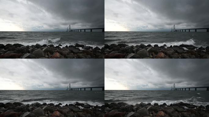 丹麦连接两个海岸的大腰带大桥的航拍画面。在横跨地平线的Storebælt桥前，巨浪冲击着石头。