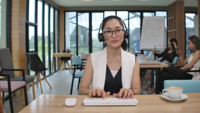 商务女性专注于电脑屏幕和耳机前的工作，在办公室的工作生活方式