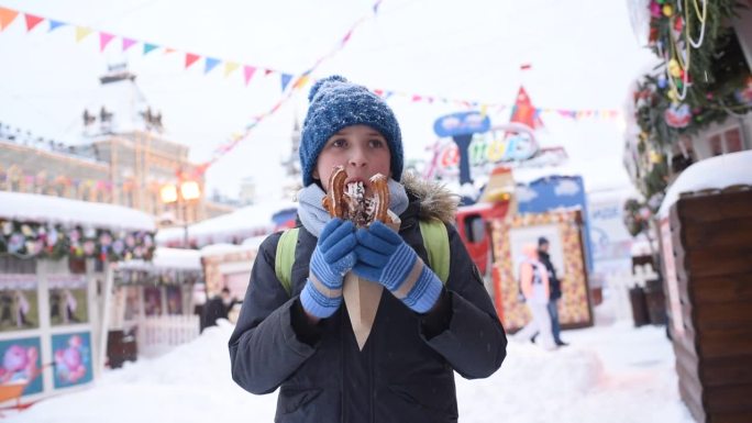 在一个下雪的冬日，穿着冬装的男孩、孩子、学生、游客在圣诞市场吃油条。