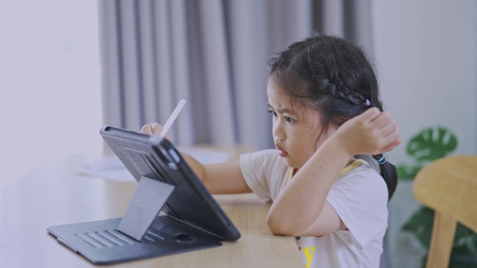 亚洲小女孩正在使用数字笔和触摸平板电脑显示屏。宝宝笑逗的时候用平板。看屏幕时间太长。可爱女孩边看电视