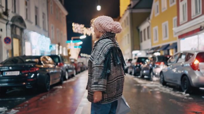 圣诞夜，穿着暖和衣服、戴着针织帽的快乐女子在城市街道中央边走边唱歌