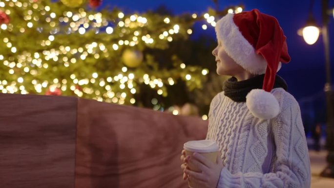 可爱的青春期前男孩在华丽的街道圣诞树旁喝着热巧克力或潘趣酒。一个快乐的孩子在镇广场的集市上庆祝平安夜