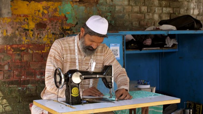 印度穆斯林男子在缝纫机上缝制衣服，戴着头盖帽的男子，低薪工人，自雇