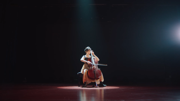 大学生穿着礼服在舞台的聚光灯下表演大提琴