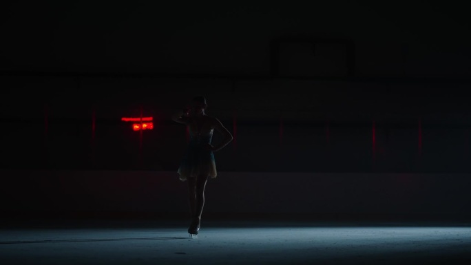 在黑暗的溜冰场上独自滑冰的女运动员，慢镜头，黑暗中的女性剪影
