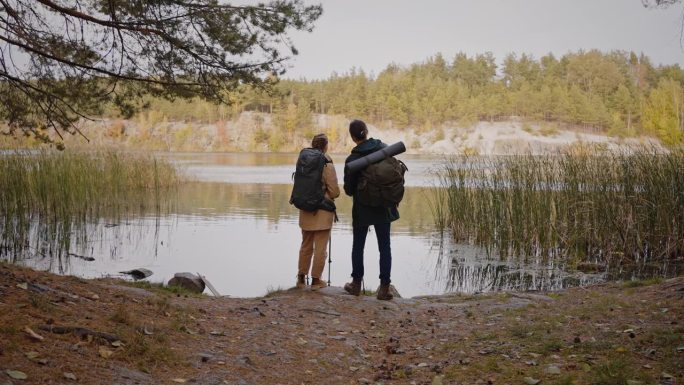 一对夫妇背着双肩包在水边欣赏秋天的风景