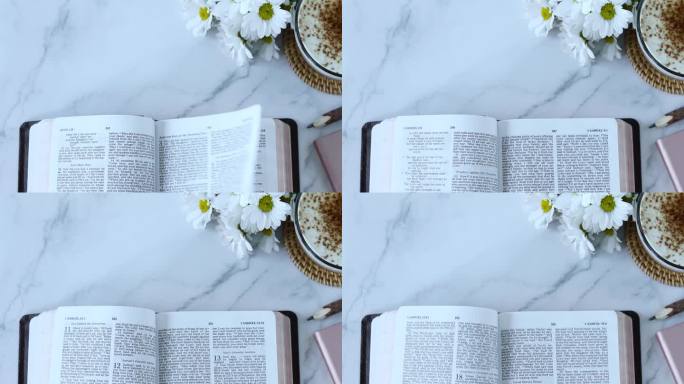 手翻页打开圣经书与一杯咖啡和鲜花在白色大理石背景，俯视图