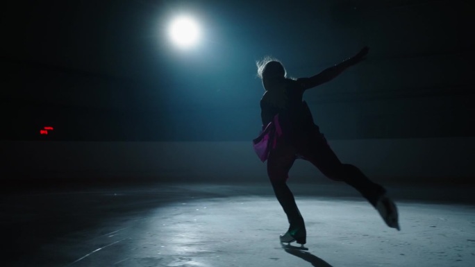 天才少年花样滑冰女孩在黑暗中的溜冰场训练，年轻的女运动员跳跃