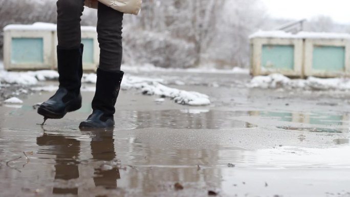 女孩穿着冬靴在冰冻的泥泞水坑上踩破薄冰