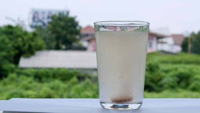 窗台上一个盛满水的玻璃杯正在冒泡，杯子底部有一片碳酸氢钠抗酸剂。