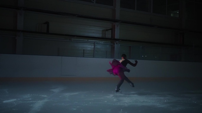 优雅的年轻女子花样滑冰运动员在黑暗中独自在溜冰场训练，女士跳跃和坠落