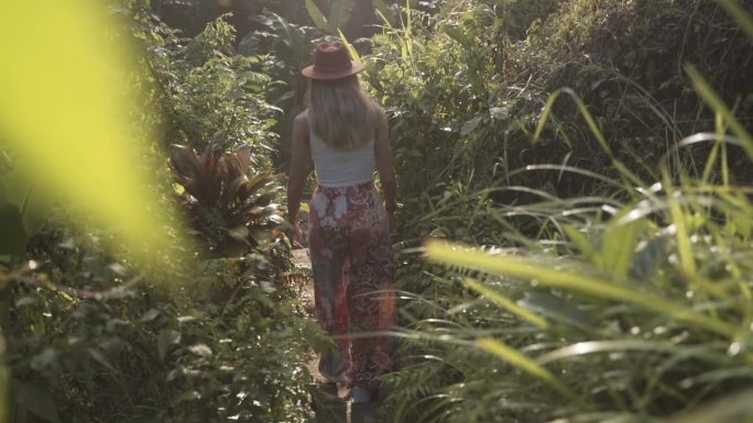 日落时分，穿着裙子、戴着太阳帽的女人穿过丛林