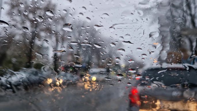 融化的雪和雨滴落在汽车的挡风玻璃上。室外景色模糊，窗外是冬季的雨夹雪