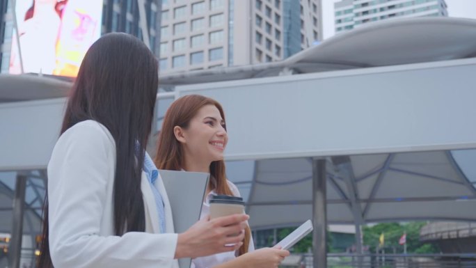 两个亚洲女商人自信地走在城市的户外。迷人美丽的女员工员工人们感到快乐和放松，同时度过闲暇时间走到办公