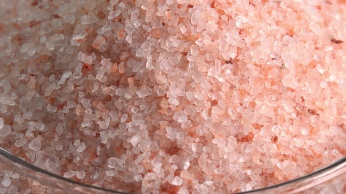 粉红色喜马拉雅盐或岩盐旋转宏观玻璃碗侧光。微量矿物质盐用于烹饪和食物展示，装饰灯和水疗