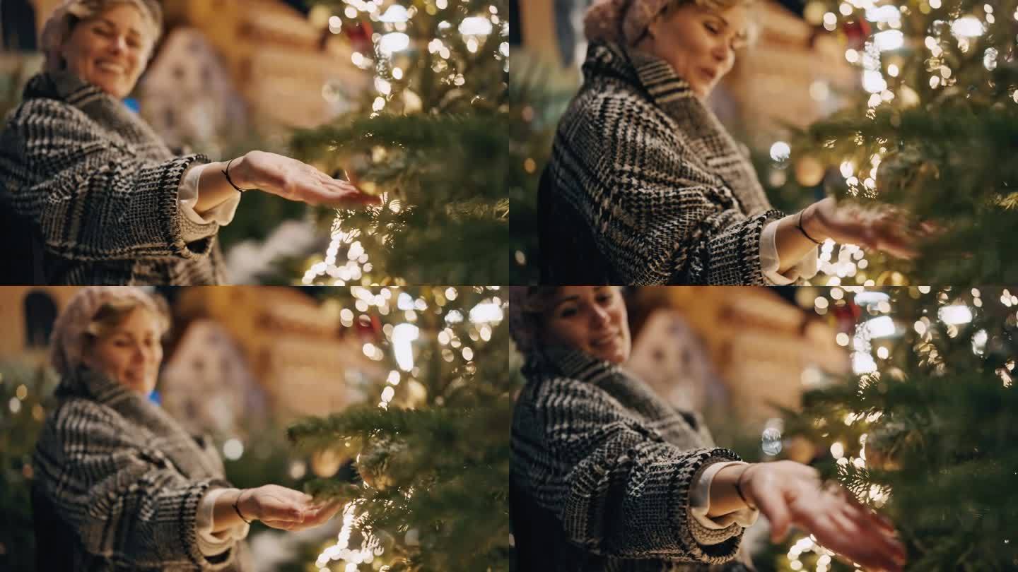 夜景中，穿着保暖衣服微笑的女人抚摸着挂在圣诞树上的小玩意