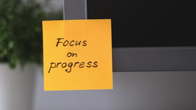 办公室的显示器上贴着一张黄色的纸条，上面写着“关注进步”的提醒。