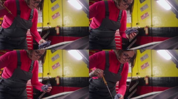 女机械师在汽车修理店用蘸油棒检查机油
