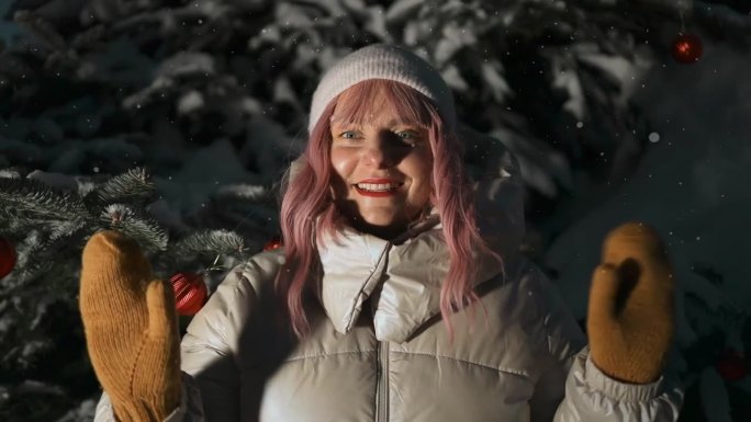 快乐的年轻粉红头发的女人走在冬天的森林里，在冬天的公园里挥舞着手臂