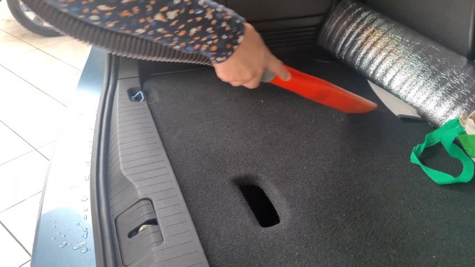 一名无法辨认的白人妇女在洗完一辆无法辨认的汽车后，用吸尘器清理她的后备箱