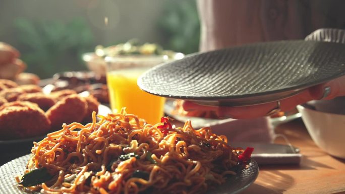 餐桌上的新鲜亚洲美食特写。以东方产品为原料的亚洲烹饪配方概念。水果饮料杯与女人手拿竹签炒面的看法