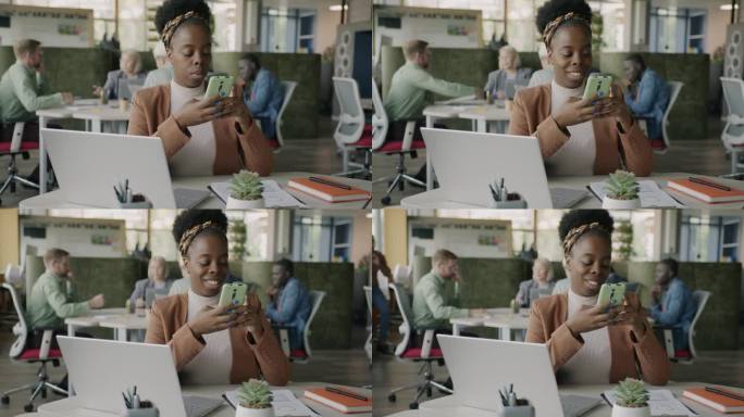 快乐的非洲裔美国女士使用智能手机短信享受现代通信在开放的空间办公室