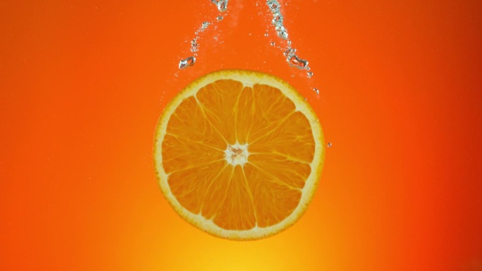 橙子落入水中的超级慢动作，孤立在橙色背景上。