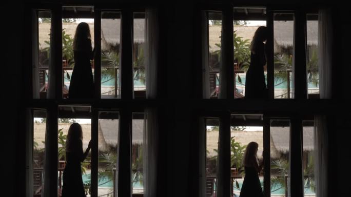 穿着黑色连衣裙的女人在阳台上放松，俯瞰着游泳池和丛林