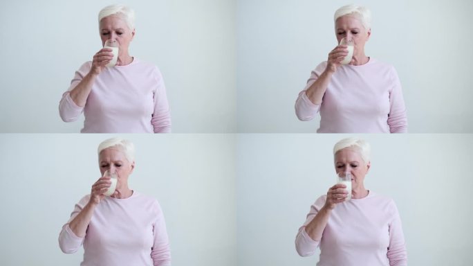 白种老年妇女从白色背景的玻璃杯中啜一口牛奶