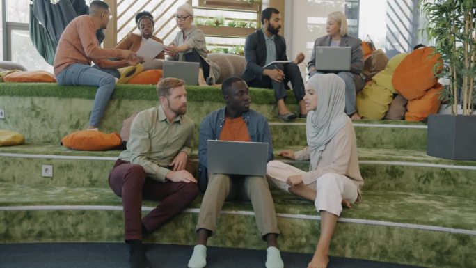 男女创意团队在舒适的共同工作空间讨论想法，并使用笔记本电脑