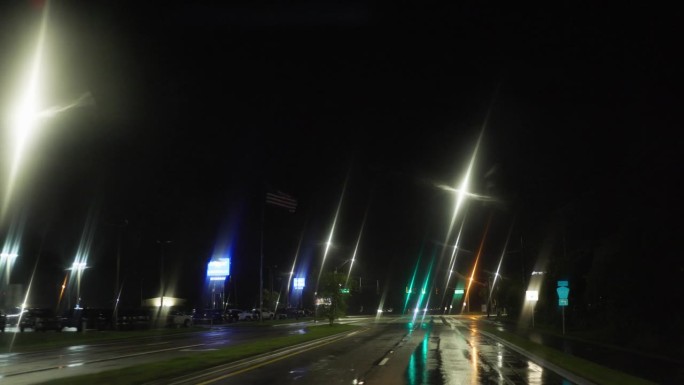 夜间沿着积水的街道行驶。在佛罗里达州坦帕湾，红灯亮起，然后在暴雨中继续前进。道路POV
