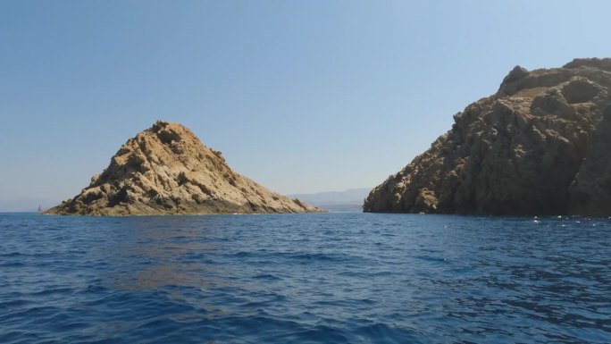 夏天，从法国鲁斯岛的一艘观光船上看到的山脉、岩石、海水和帆船。