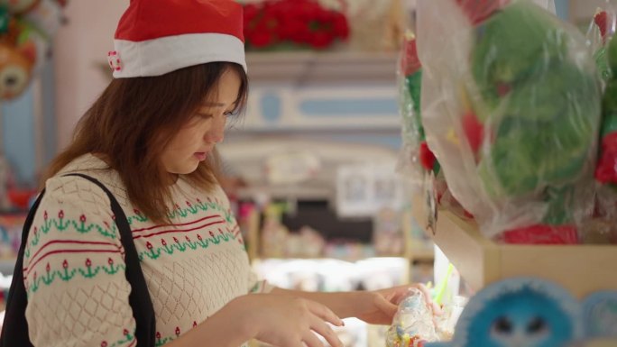 年轻的亚洲妇女戴着圣诞老人的帽子为圣诞节挑选圣诞礼物。女士在挑选圣诞装饰用品。圣诞节的庆祝活动。圣诞