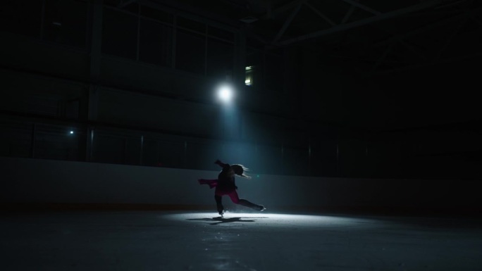 职业女子花样滑冰运动员在黑暗的溜冰场上旋转，变焦镜头