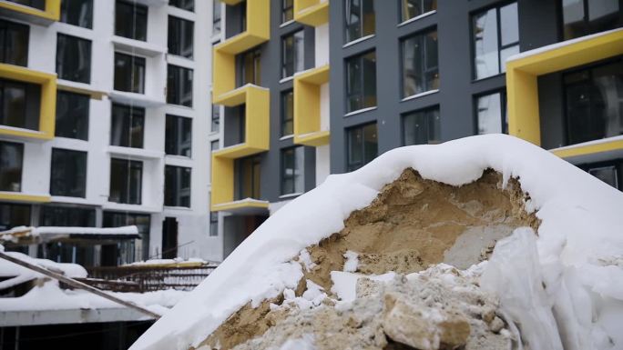 冬季施工区域上的沙堆。积雪下覆盖着一堆沙子，背景是未完工的建筑