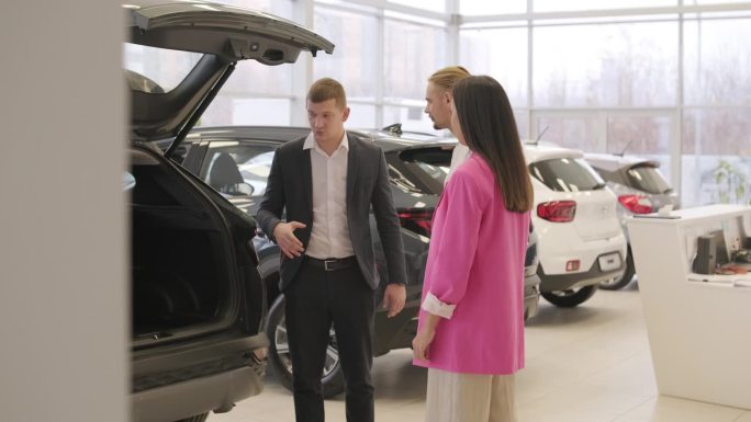在经销商沙龙上，年轻的汽车推销员向年轻夫妇展示新车。