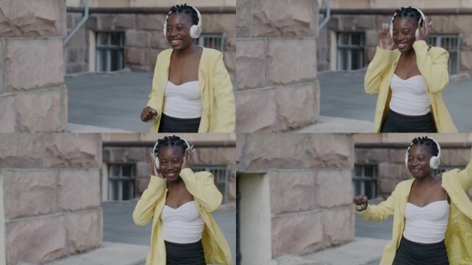 快乐的非裔美国女士走在城市的街道上，戴着耳机听音乐跳舞