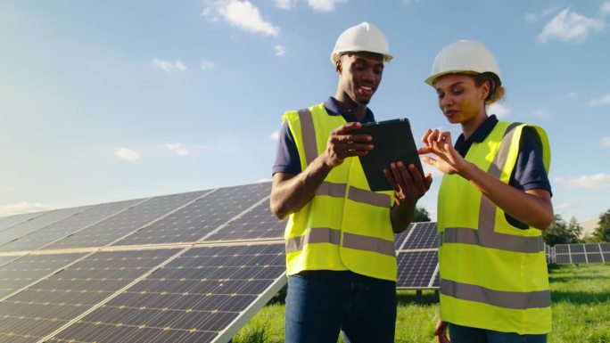 拿着数码平板电脑的男女工程师正在检查产生可再生能源的太阳能电池板