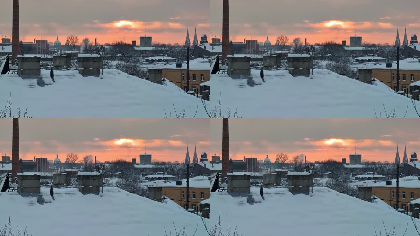 在城市工业区的屋顶上，雪花缓缓落下，太阳在灰色的冬日天空中发出橙色的光芒